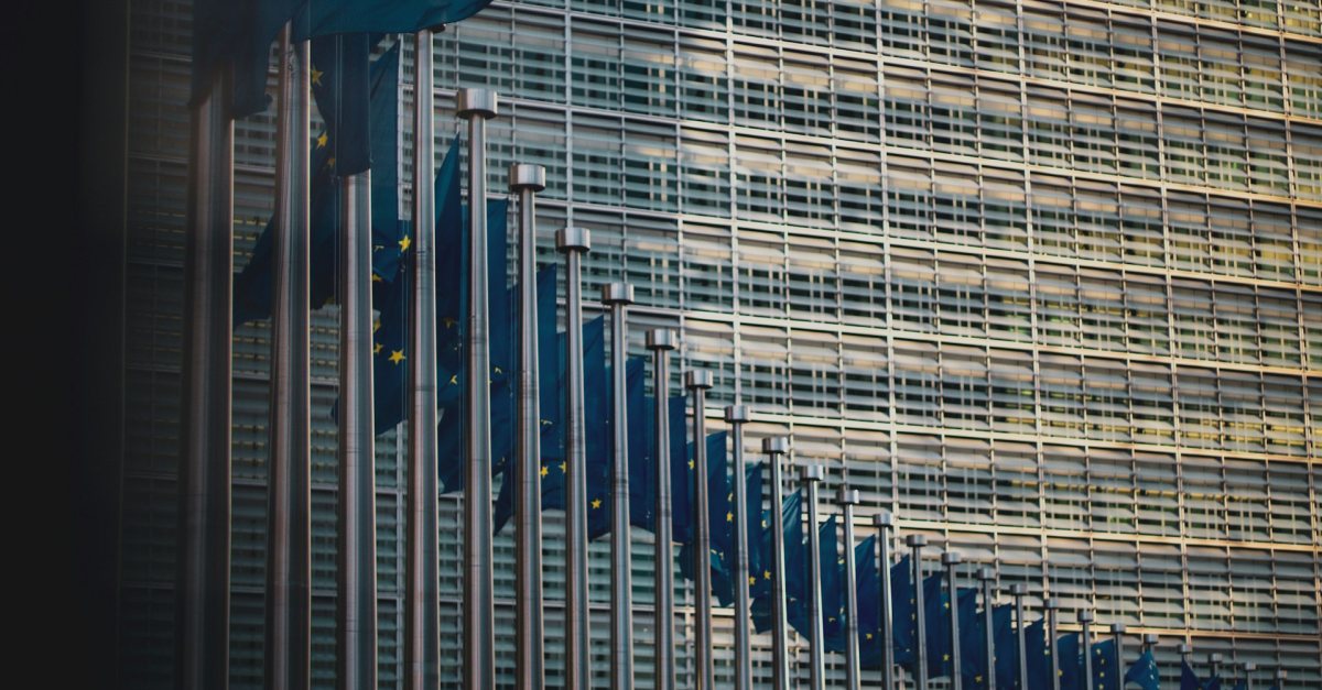 A row of European Union flags in front of the glass façade of the Berlaymont building in Brussels