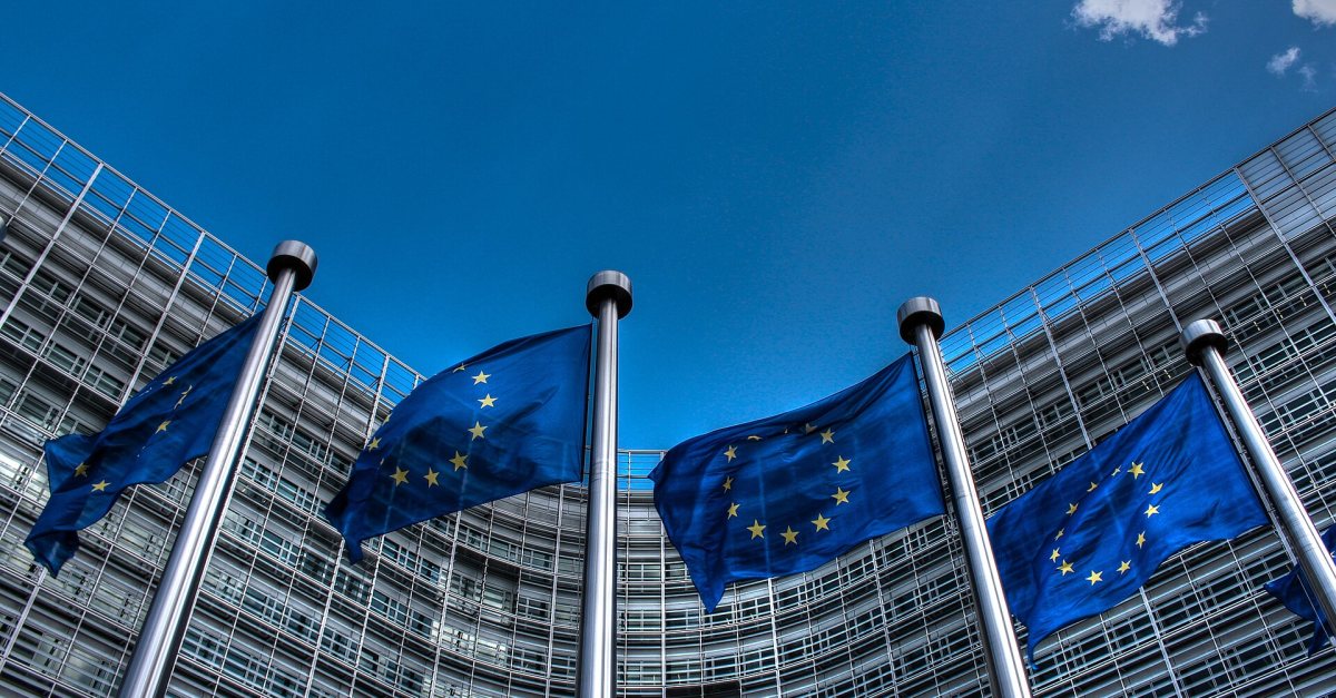 European Union flags flying in front of the Berlaymont building in Brussels under a blue sky